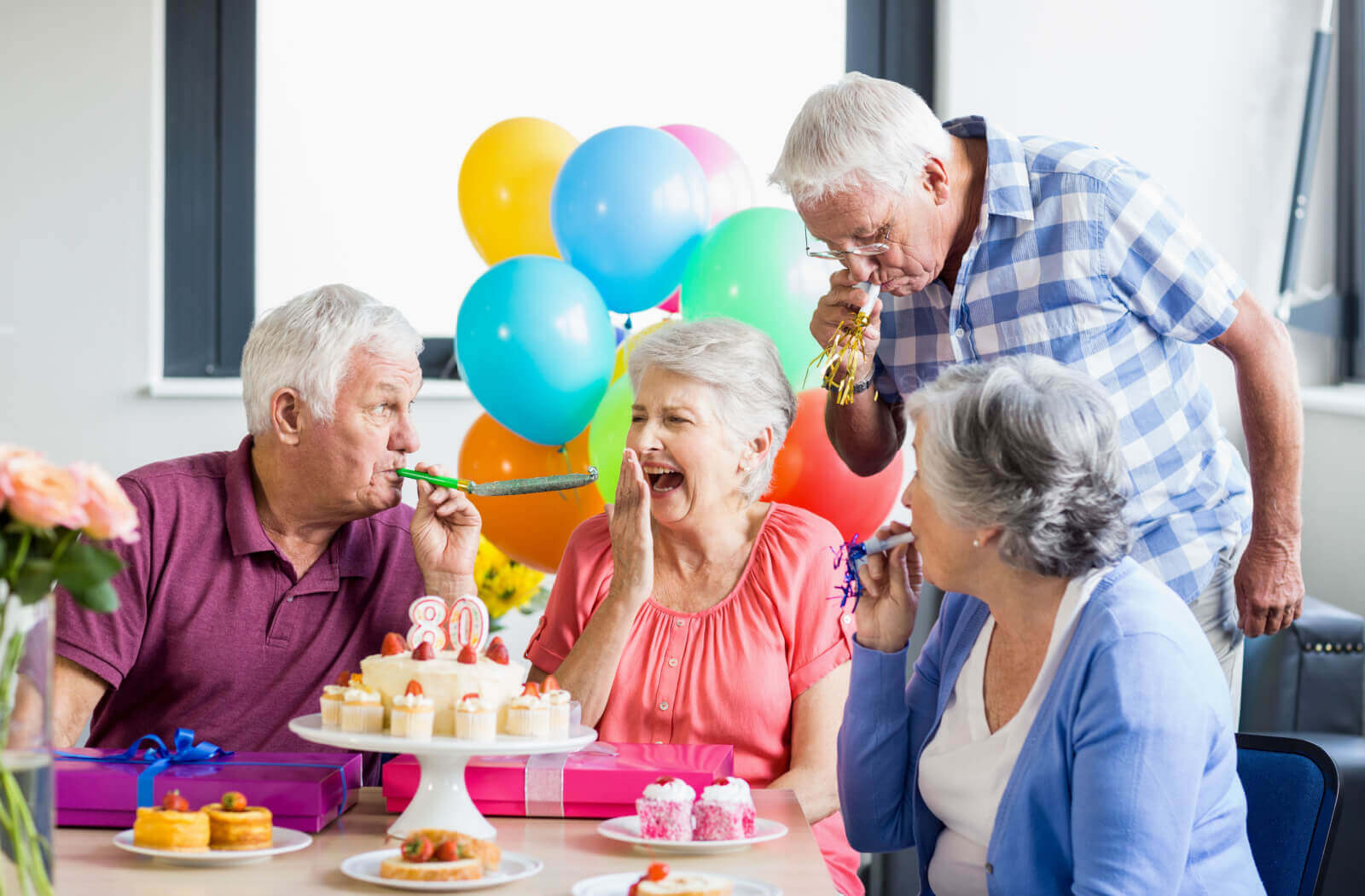 A senior woman and her friends blowing streamers with cupcakes celebrating her 80th birthday in assisted living.