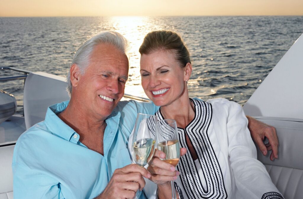 A happy retired couple clinks champagne glasses together while sitting on the back of a boat at sunset on a Florida bay