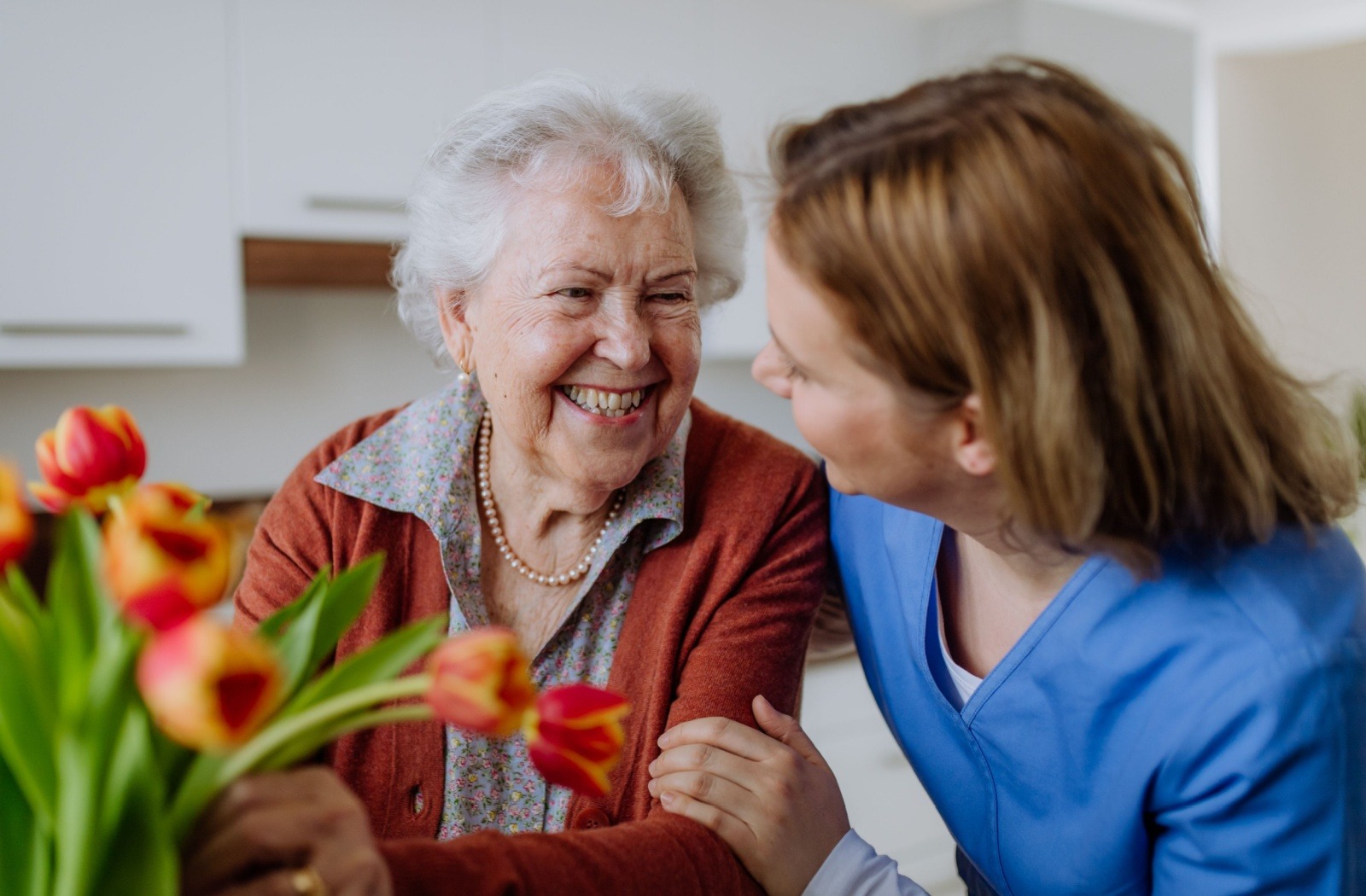 A caregiver gently supports a senior as they arrange a bouquet of flowers.