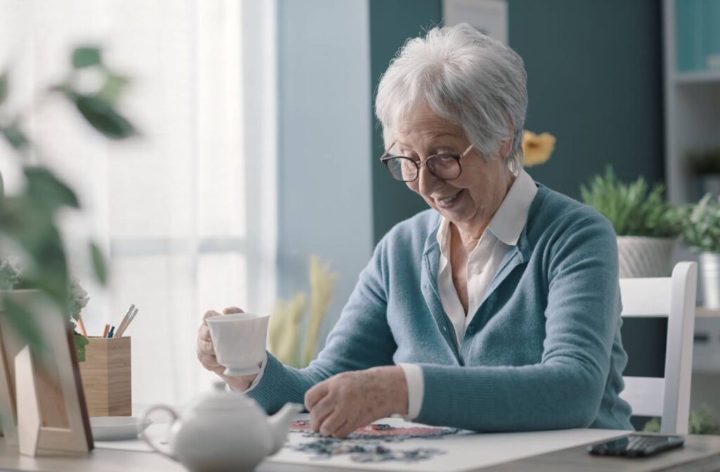 a senior sits at a table drinking a coffee and doing a puzzle